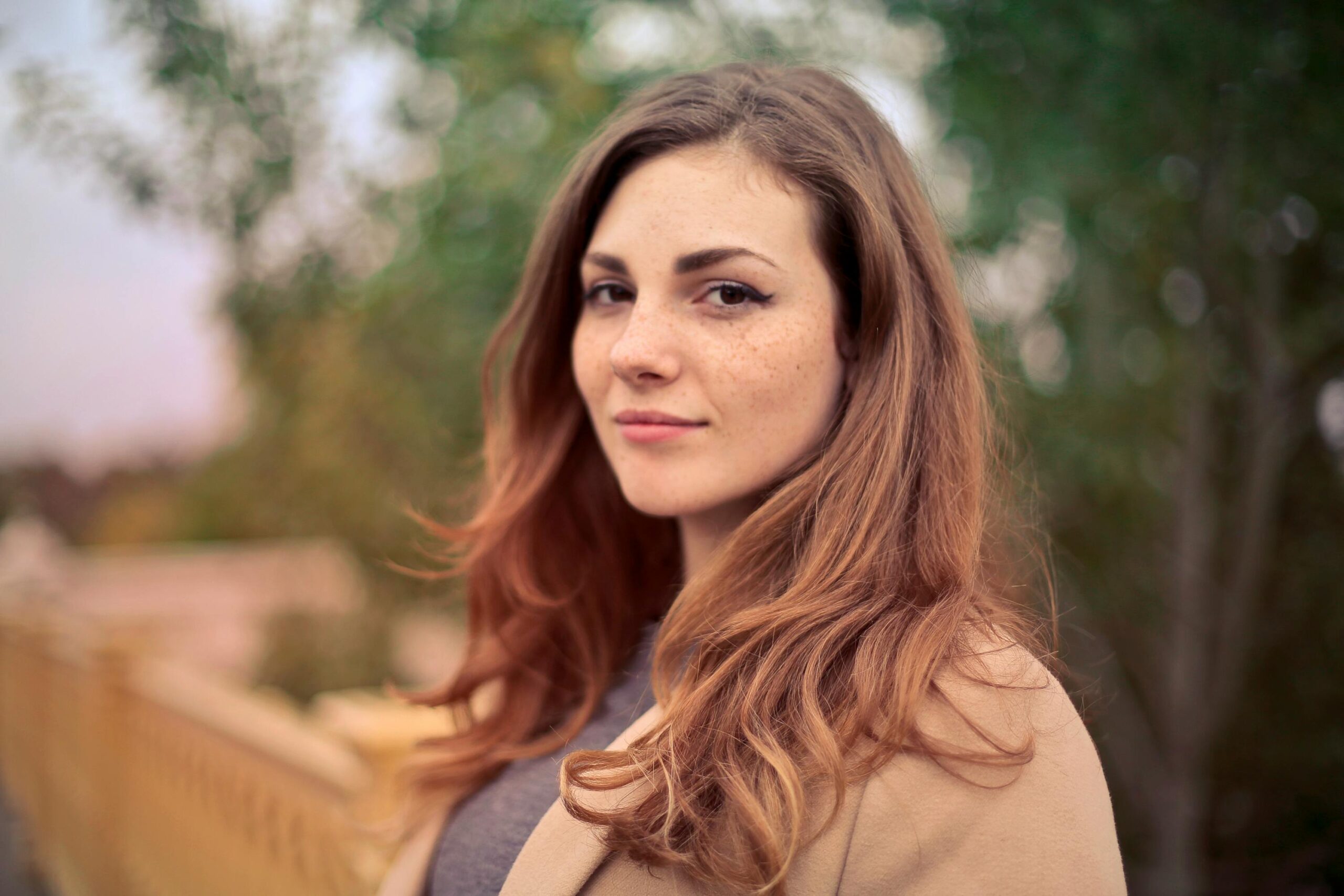 A young woman with long hair smiles confidently for an outdoor portrait session.